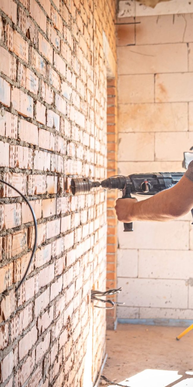 Handyman at a construction site in the process of drilling a wall with a perforator.