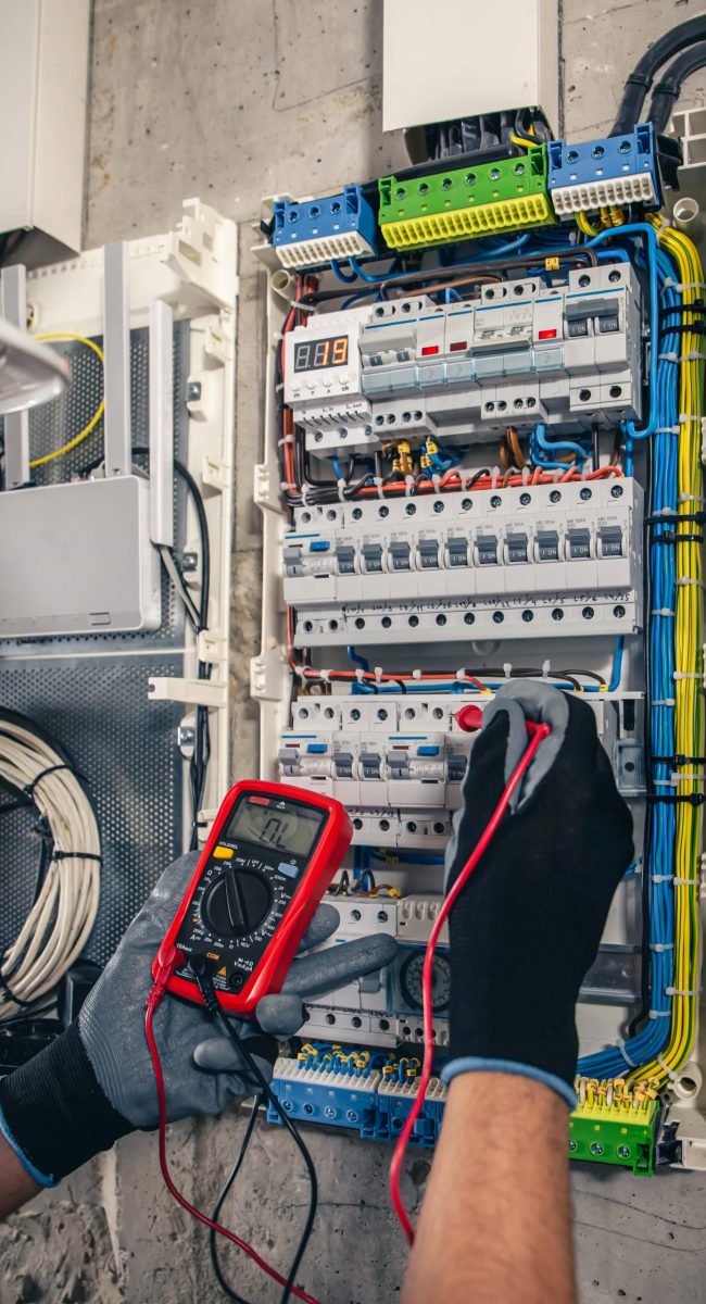 Man, an electrical technician working in a switchboard with fuses. Installation and connection of electrical equipment. Professional uses a tablet.